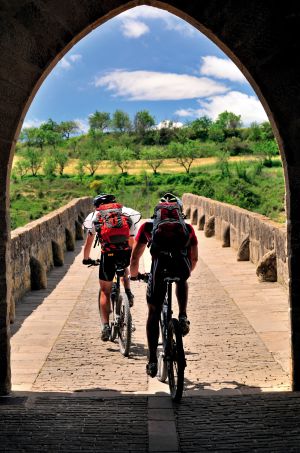 Dois ciclistas na ponte românica de Puente la Reina, na passagem do Caminho de Santiago por Navarra.